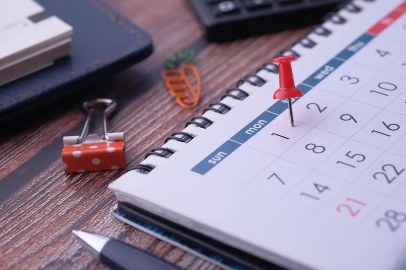 Wandkalender mit eingekreisten Terminen und einem Bleistift auf dem Schreibtisch